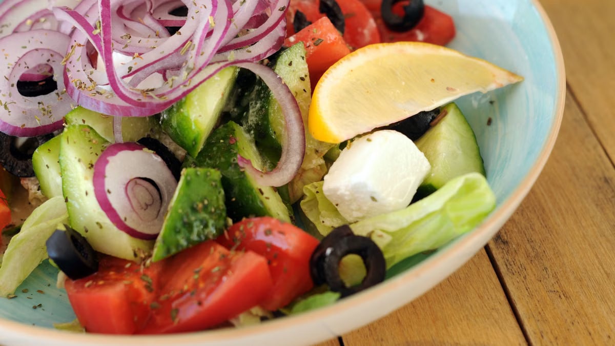 A vibrant bowl of Greek salad with fresh vegetables, feta cheese, and a lemon slice.