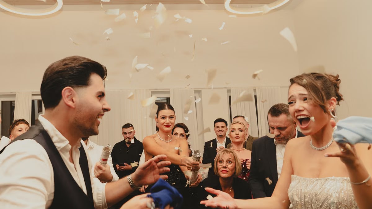 Bride and groom celebrating at a lively indoor wedding reception with friends and family.